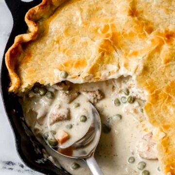 Overhead view of finished pot pie in cast iron skillet with serving spoon in it.