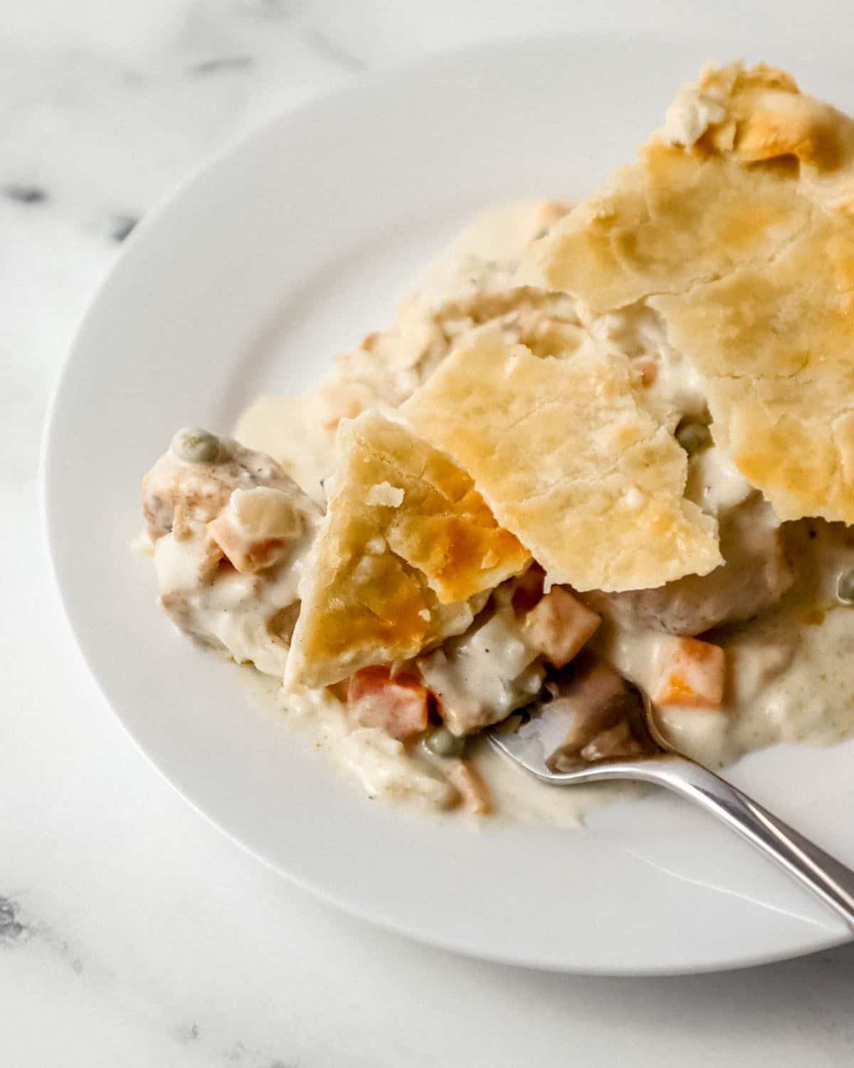 Overhead view of piece of pot pie on white plate with fork in it. 