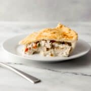 Close up side view of piece of pot pie on white plate by a fork.
