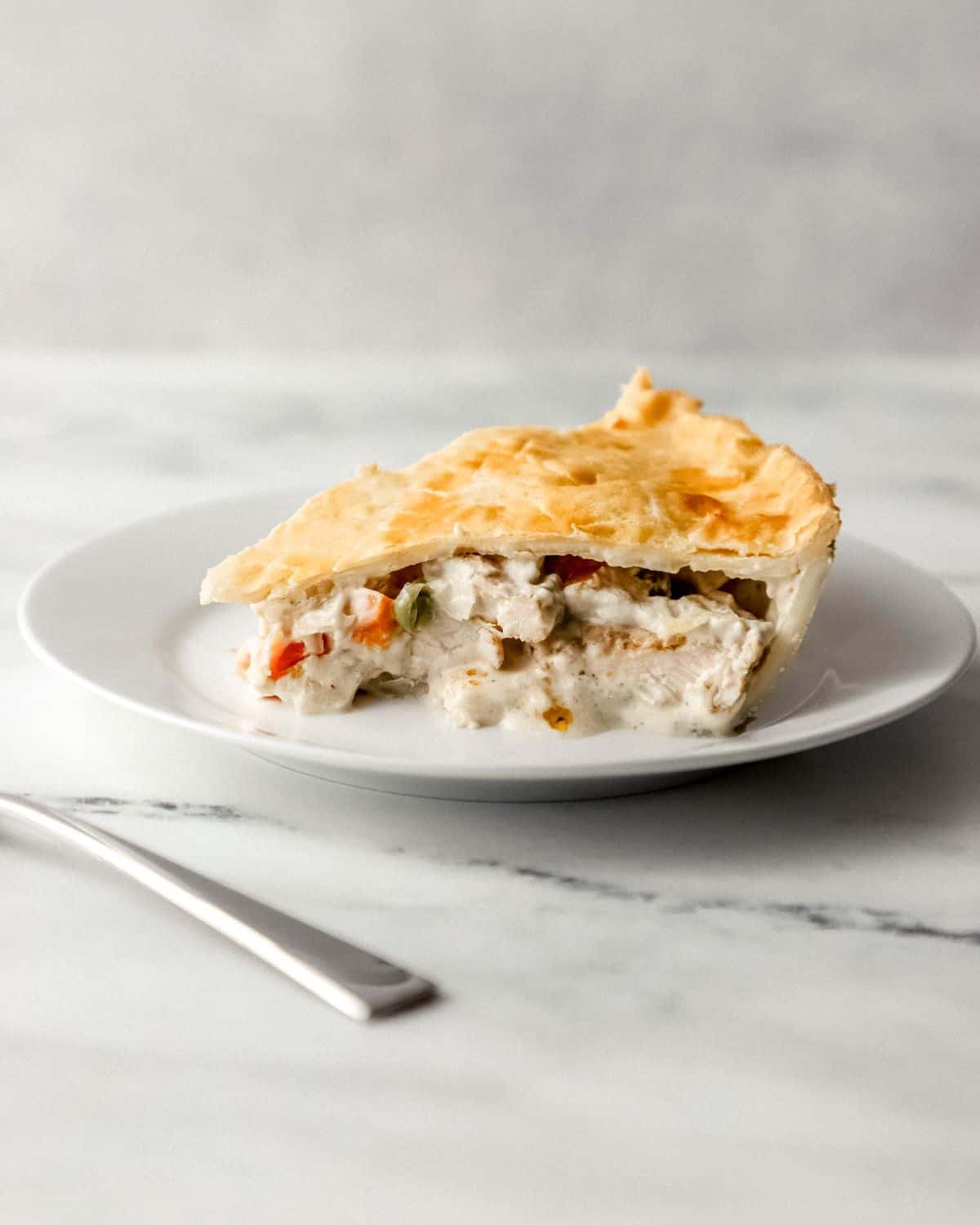 Close up side view of slice of finished pot pie on white plate by a fork. 