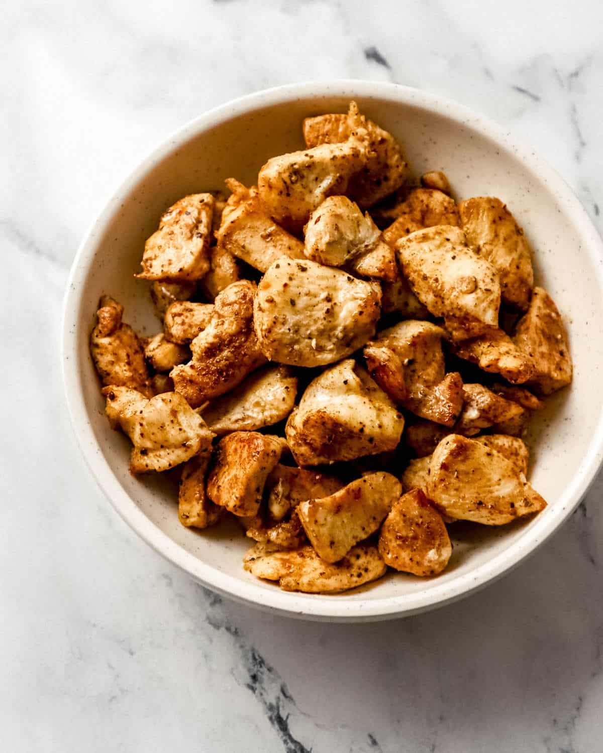 Overhead view of cooked chicken in white bowl on marble surface. 