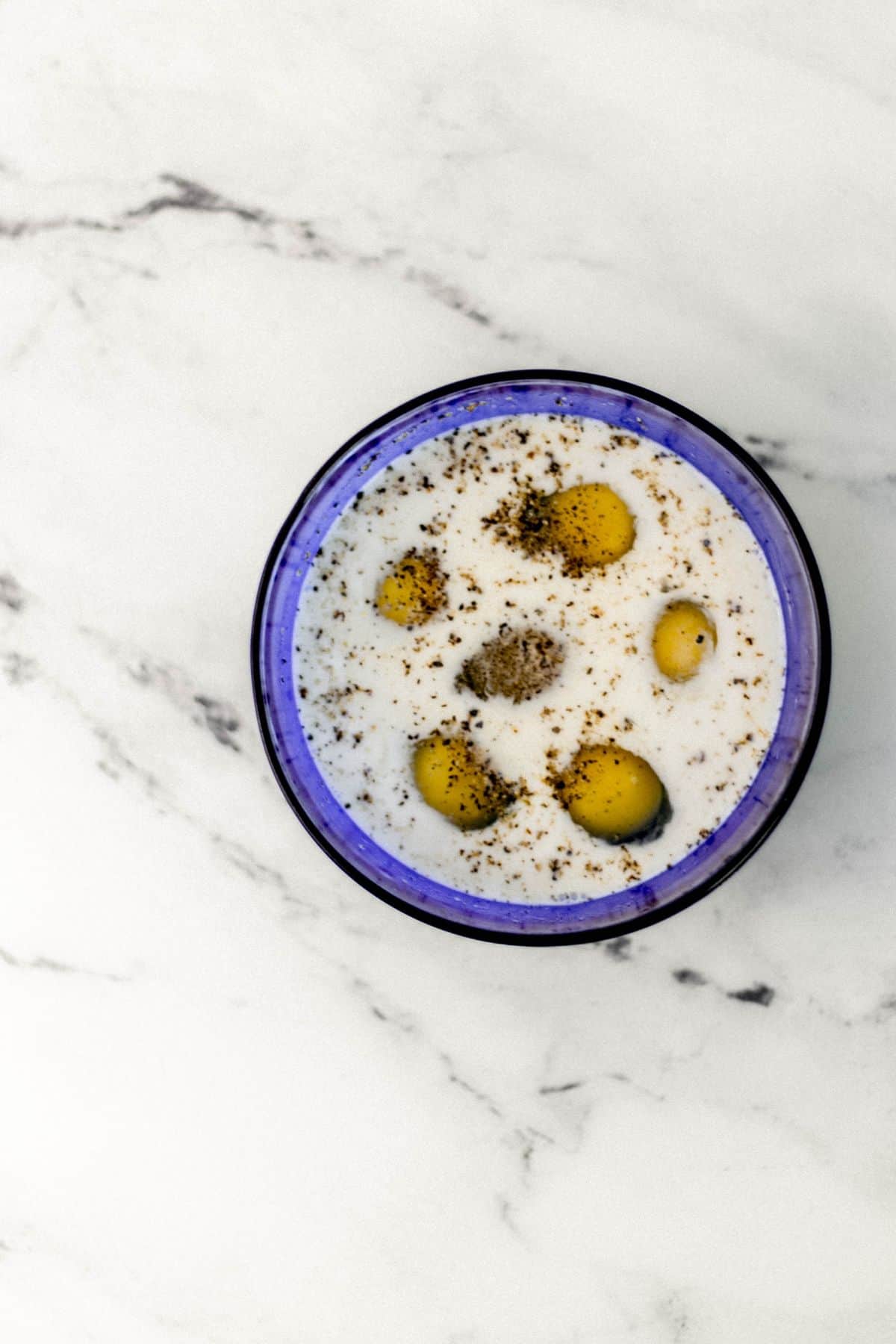 eggs, milk, salt, and pepper in small blue bowl 