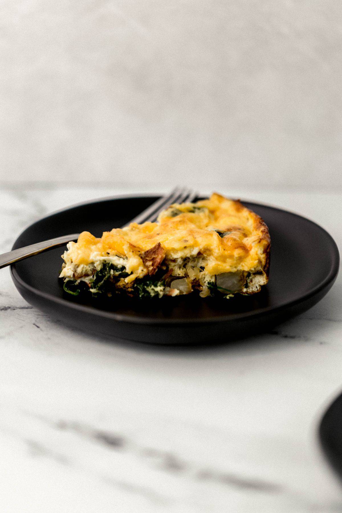 close up side view of piece of fritatta on black plate with fork 