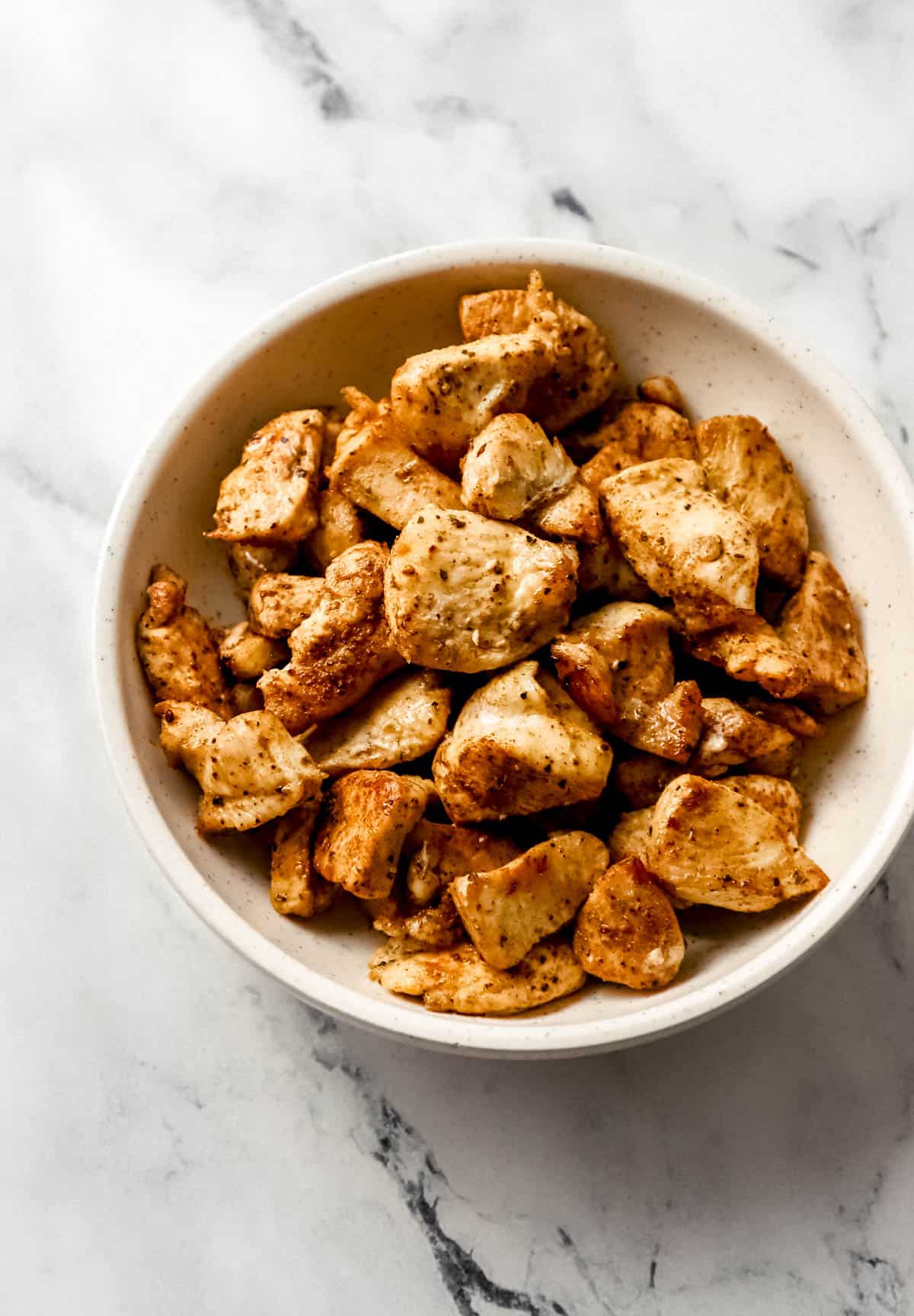 overhead view of cooked chicken in bowl on marble surface 