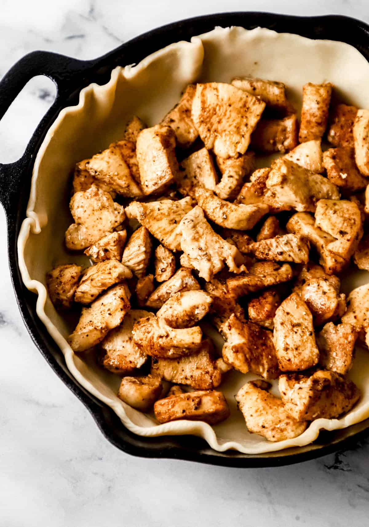 cooked chicken on top of pie crust in cast iron skillet 