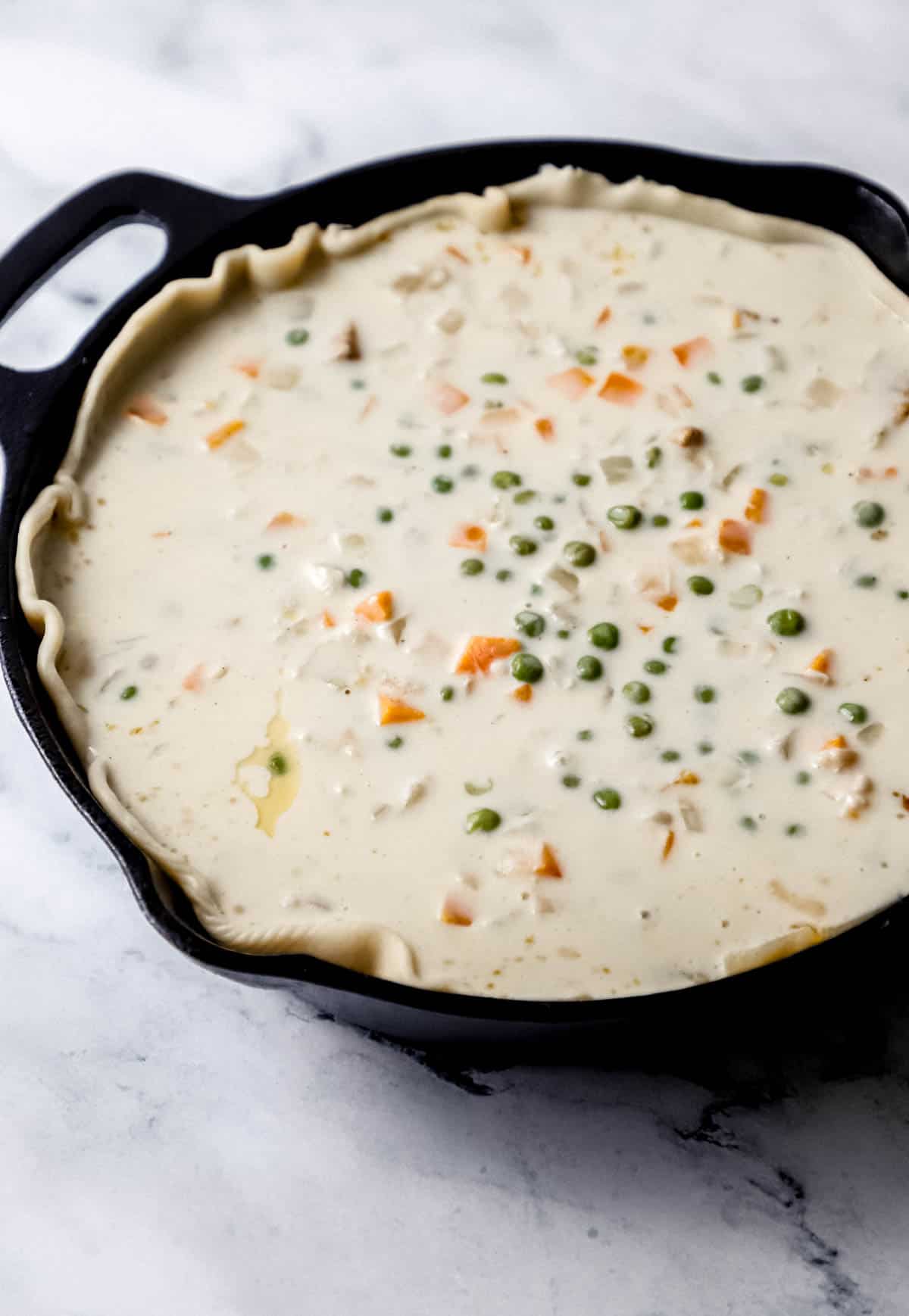sauce ingredients added to chicken and pie crust in cast iron skillet