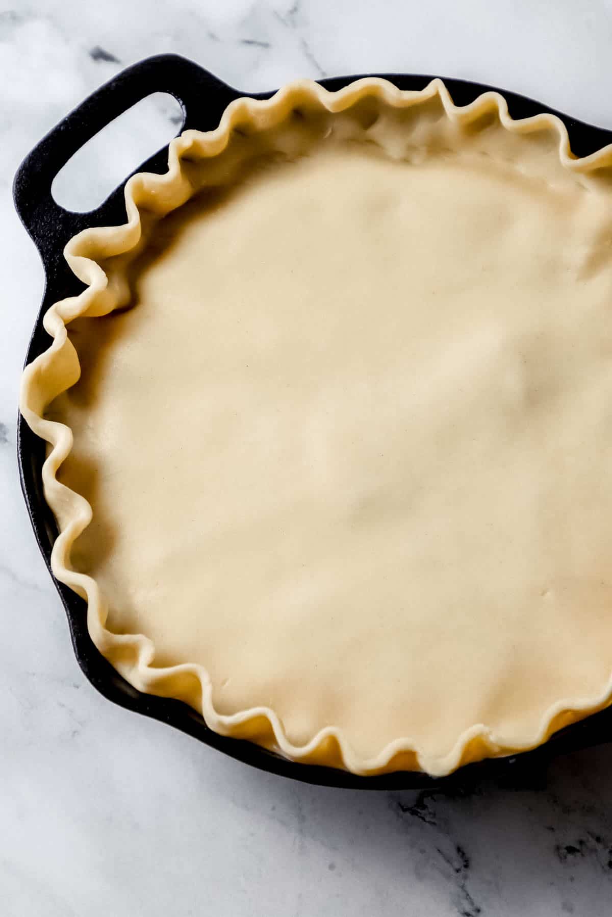 top pie crust added to the rest of the chicken pot pie ingredients in a cast iron skillet 