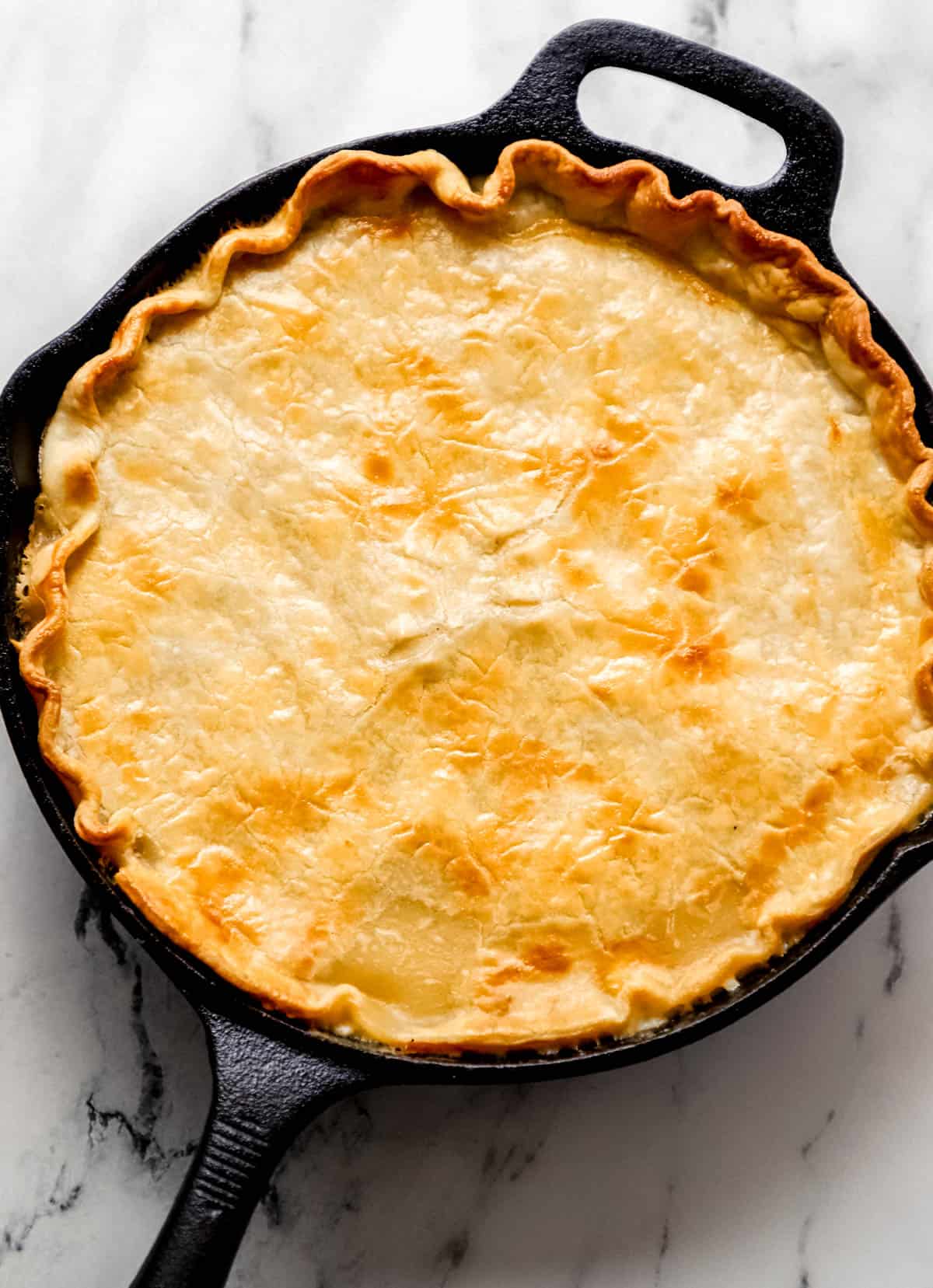 overhead view of finished chicken pot pie in cast iron skillet over marble surface 