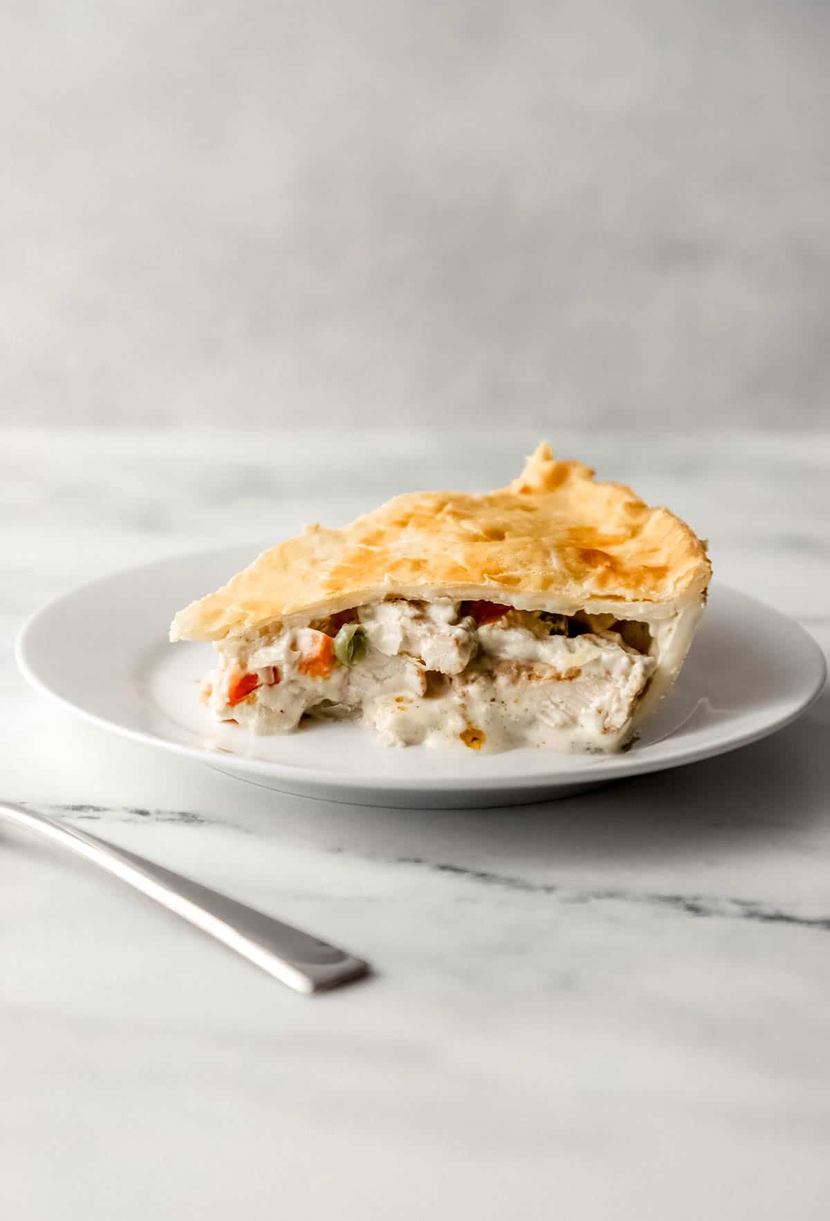 close up side view of piece of chicken pie on white plate beside a fork 