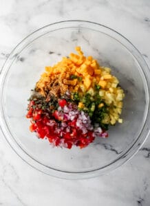 Overhead view of ingredients to make salsa added to glass mixing bowl.
