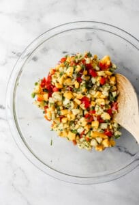 Salsa ingredients in large glass mixing bowl with wooden spoon.