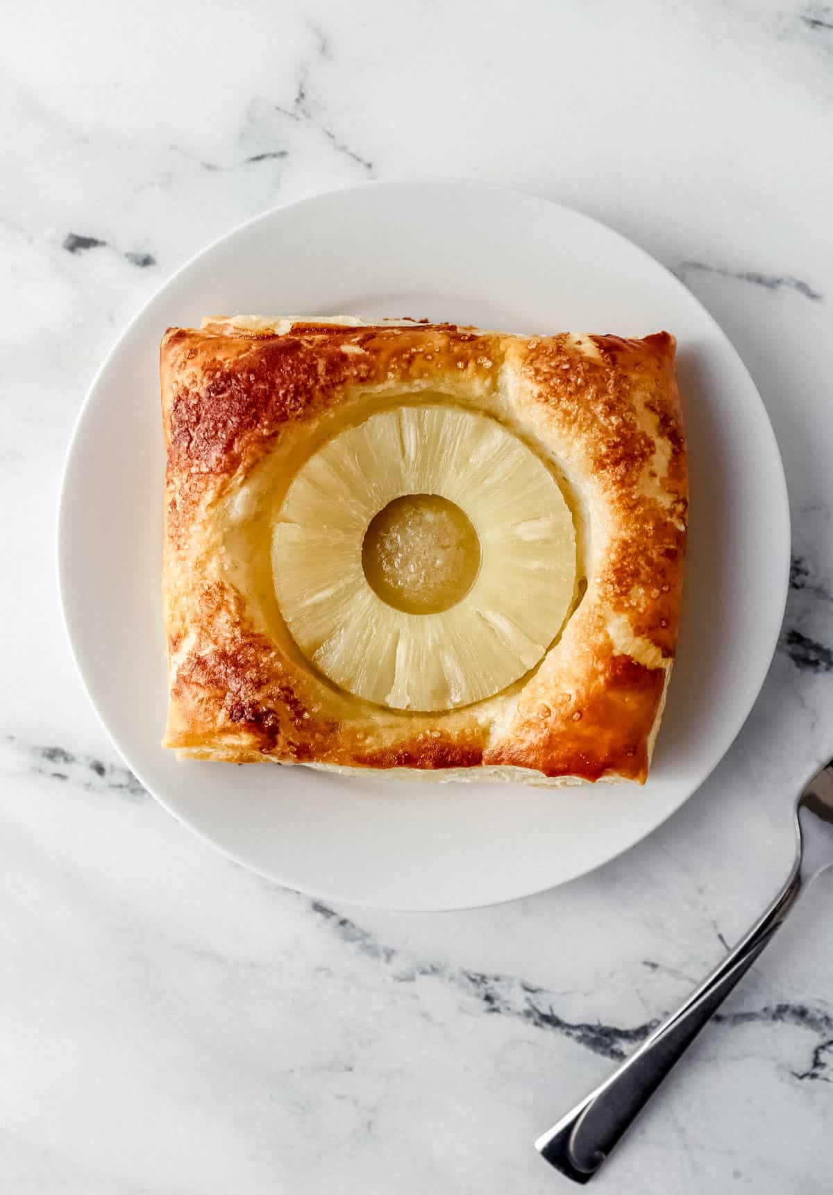 single tart on white plate beside a fork on marble surface 