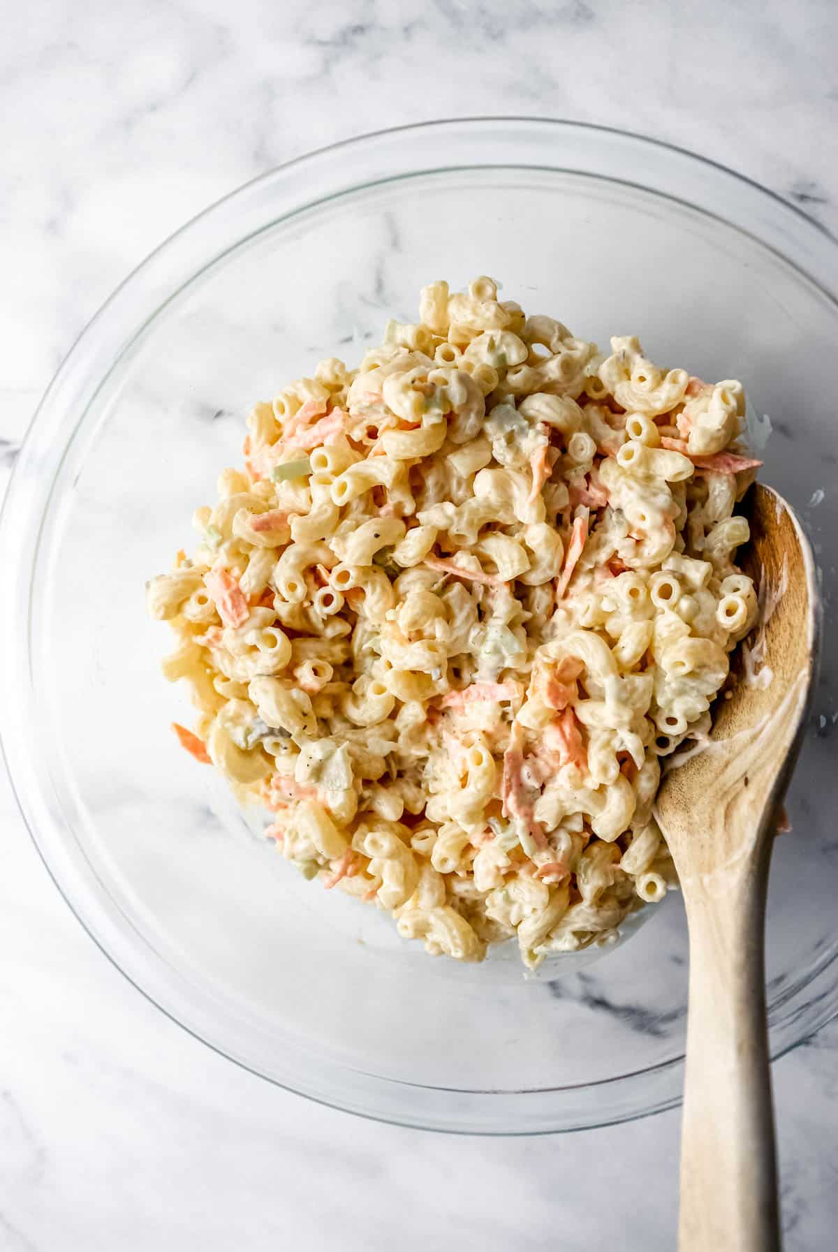 finished pasta salad in glass mixing bowl with wooden spoon 