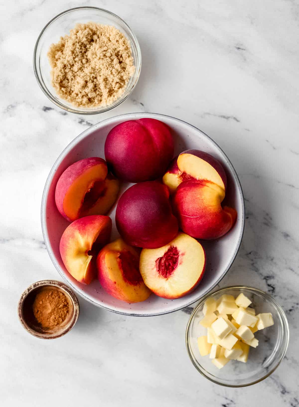 Overhead view of ingredients needed to make peach recipe in separate bowls on marble surface. 