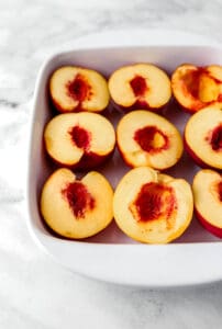Close up view of peach halved added to baking dish.