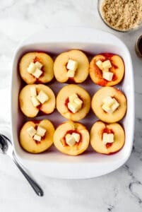 Cubed butter added to peach halved in baking dish.