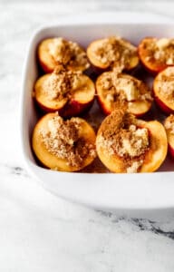 Close up view of peach halves in baking dish topped with butter and spices.