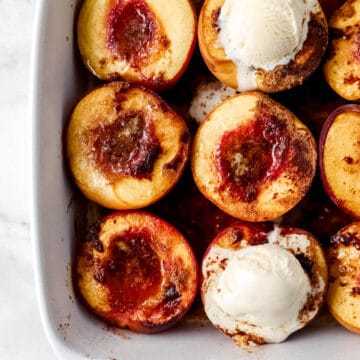 Overhead view of baked peaches in white baking dish topped with two scoops of ice cream.