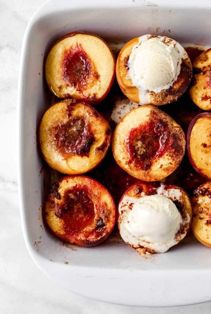 Overhead view of baked peaches in white baking dish topped with two scoops of ice cream.