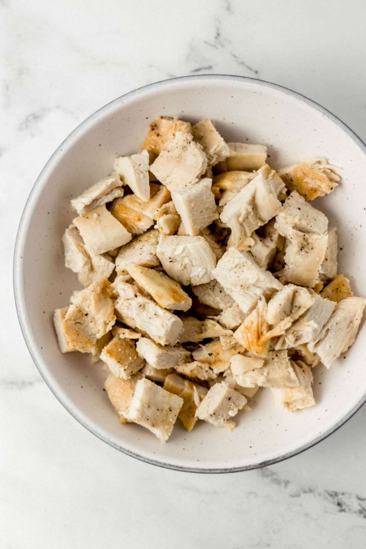 overhead view of cooked and cut up chicken in white bowl on marble surface 