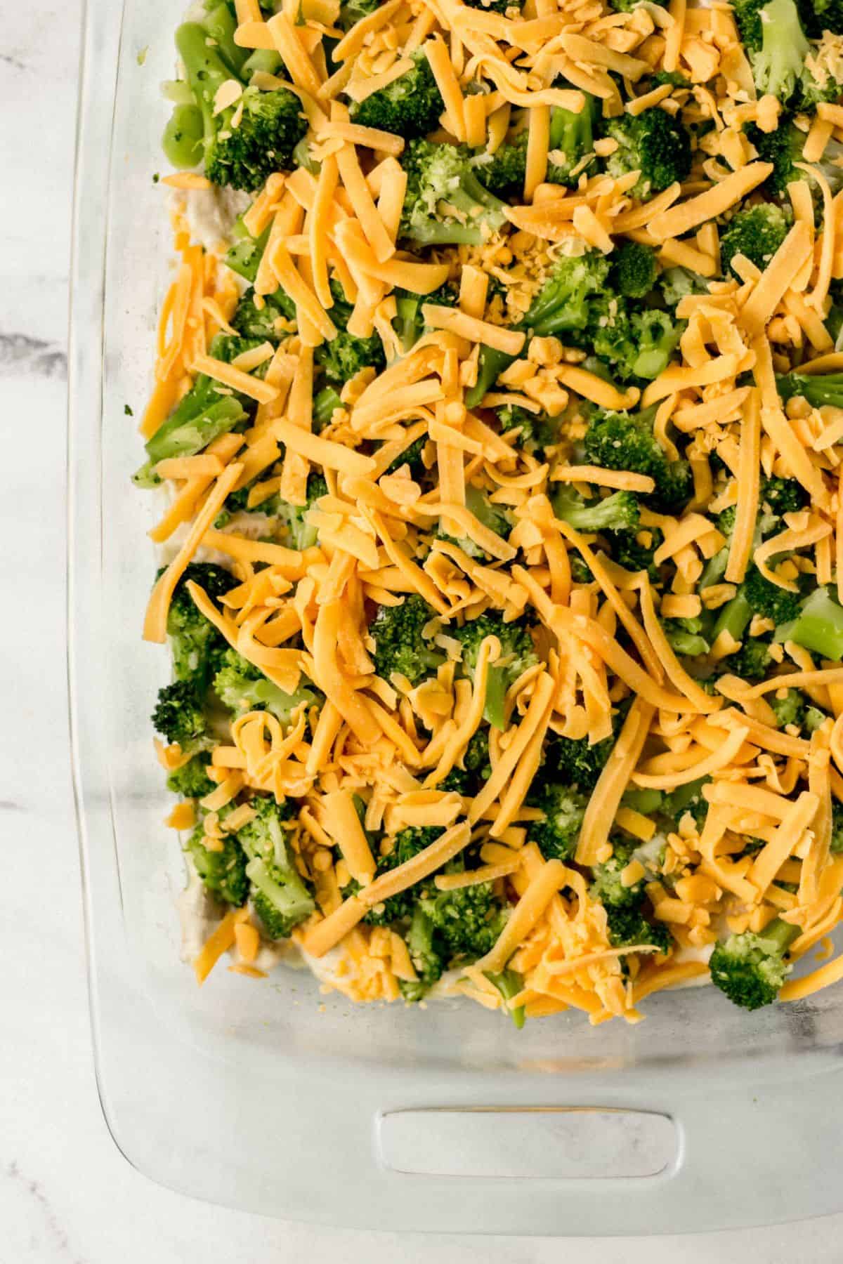 shredded cheese added to casserole with other ingredients in glass baking dish 