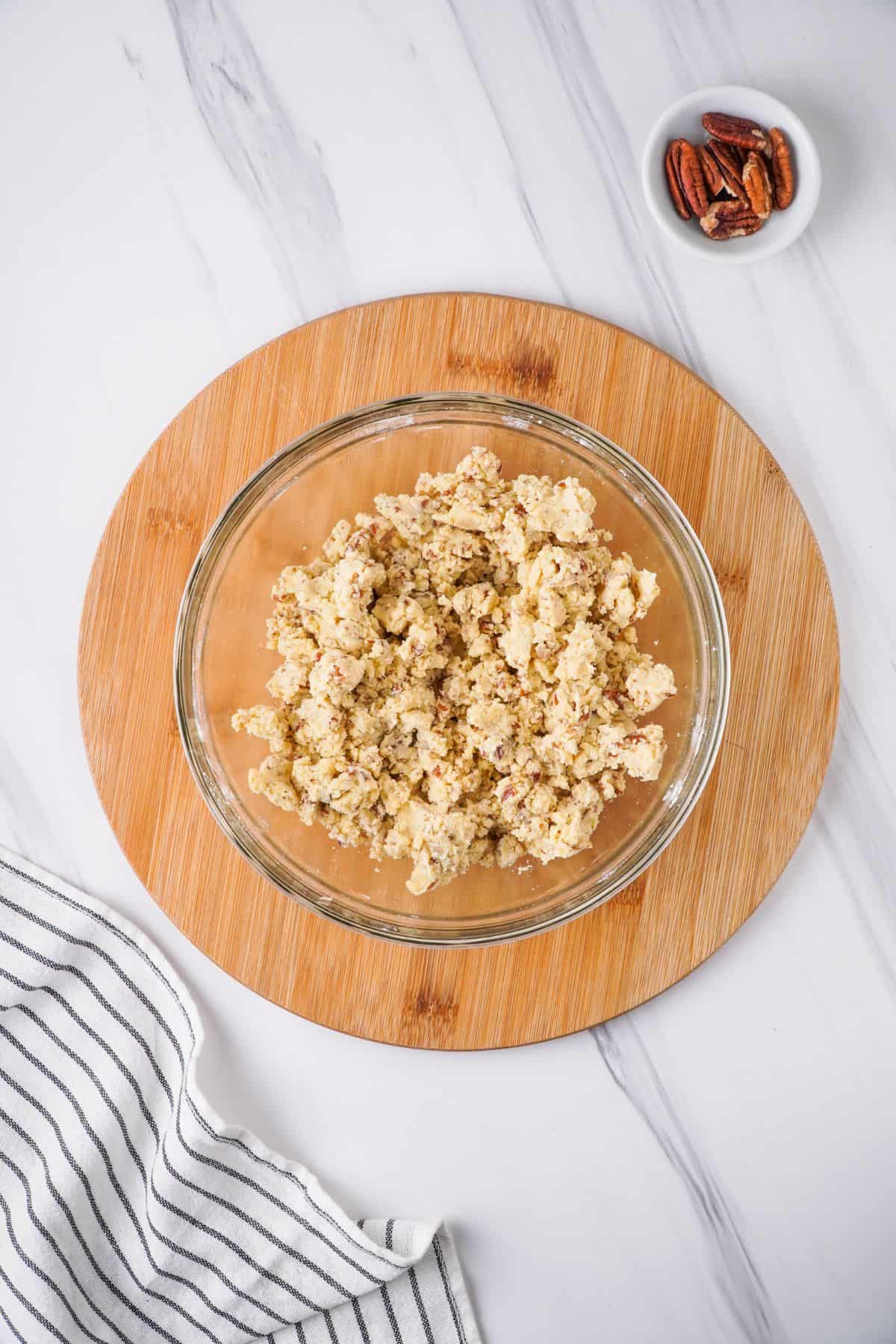 flour, pecans, salt, and butter combined in glass bowl. Small white bowl of whole pecans beside it.