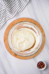 Overhead view of cream cheese layer ingredients combined in glass mixing bowl.