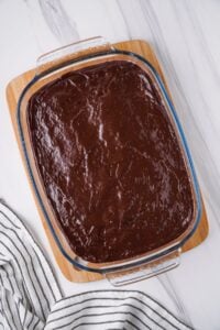 Chocolate pudding layer added to other dessert layers in glass baking dish.