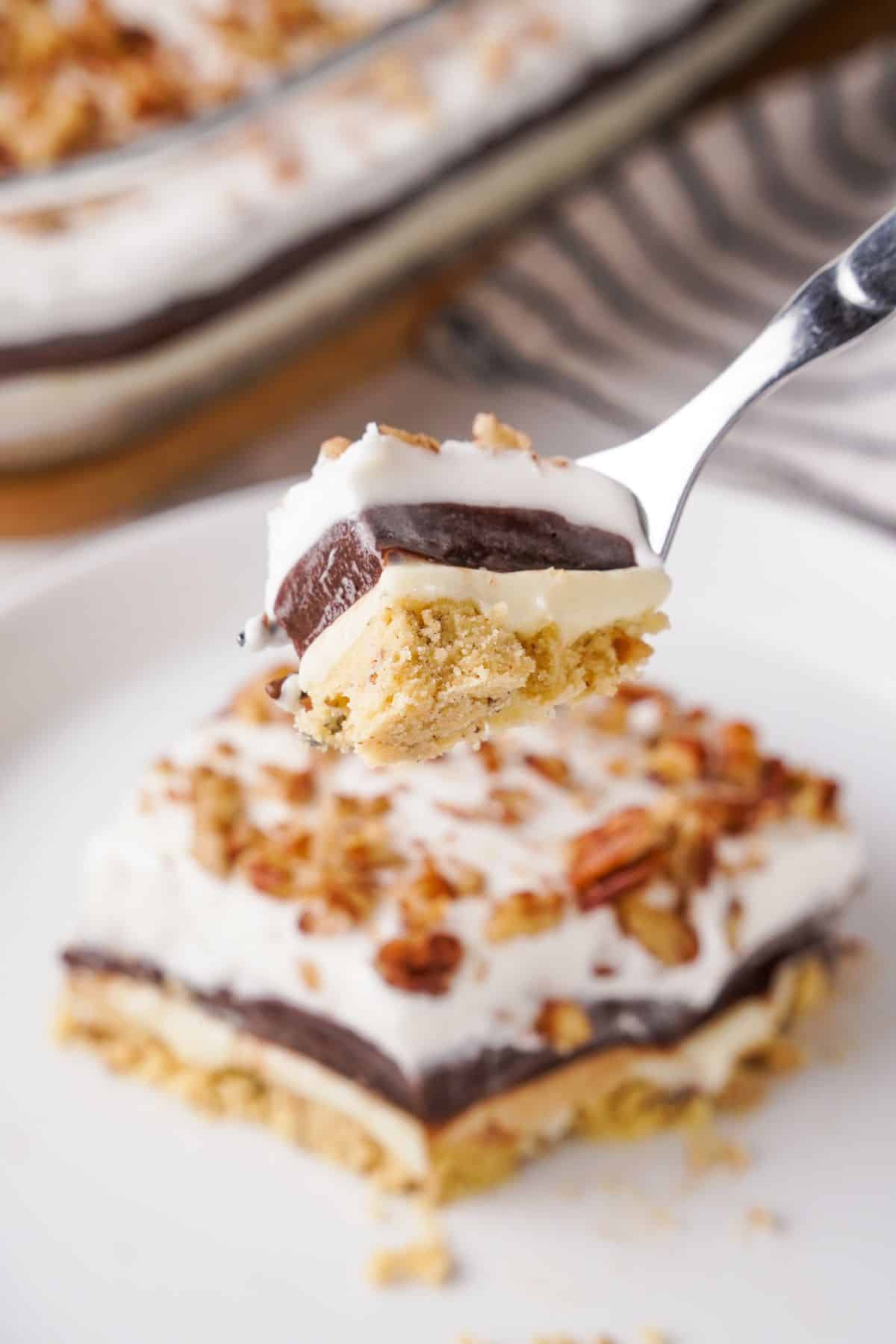 Close up of fork with dessert on it with the rest on a white plate in the background. 