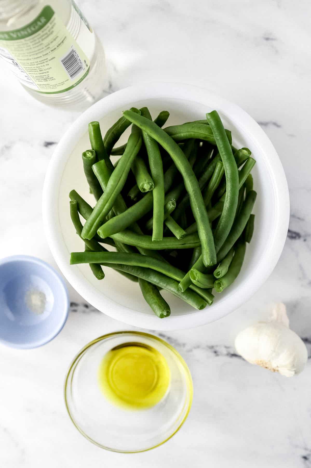 ingredients needed to make green beans in separate bowls with a bottle of vinegar and fresh garlic