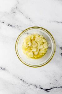 Sliced garlic in oil in small glass bowl.