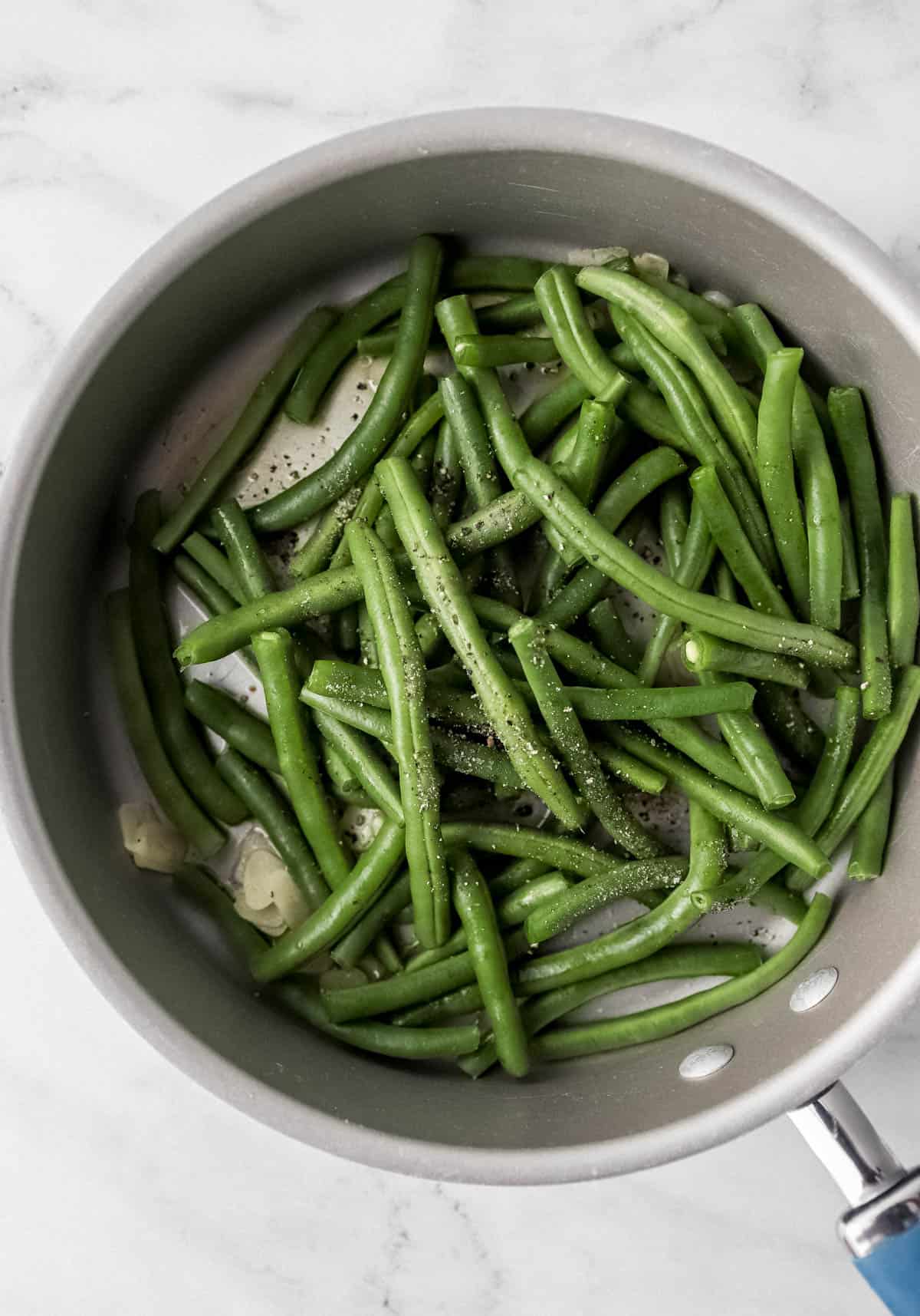 overhead view of green bean ingredients added to large skillet 