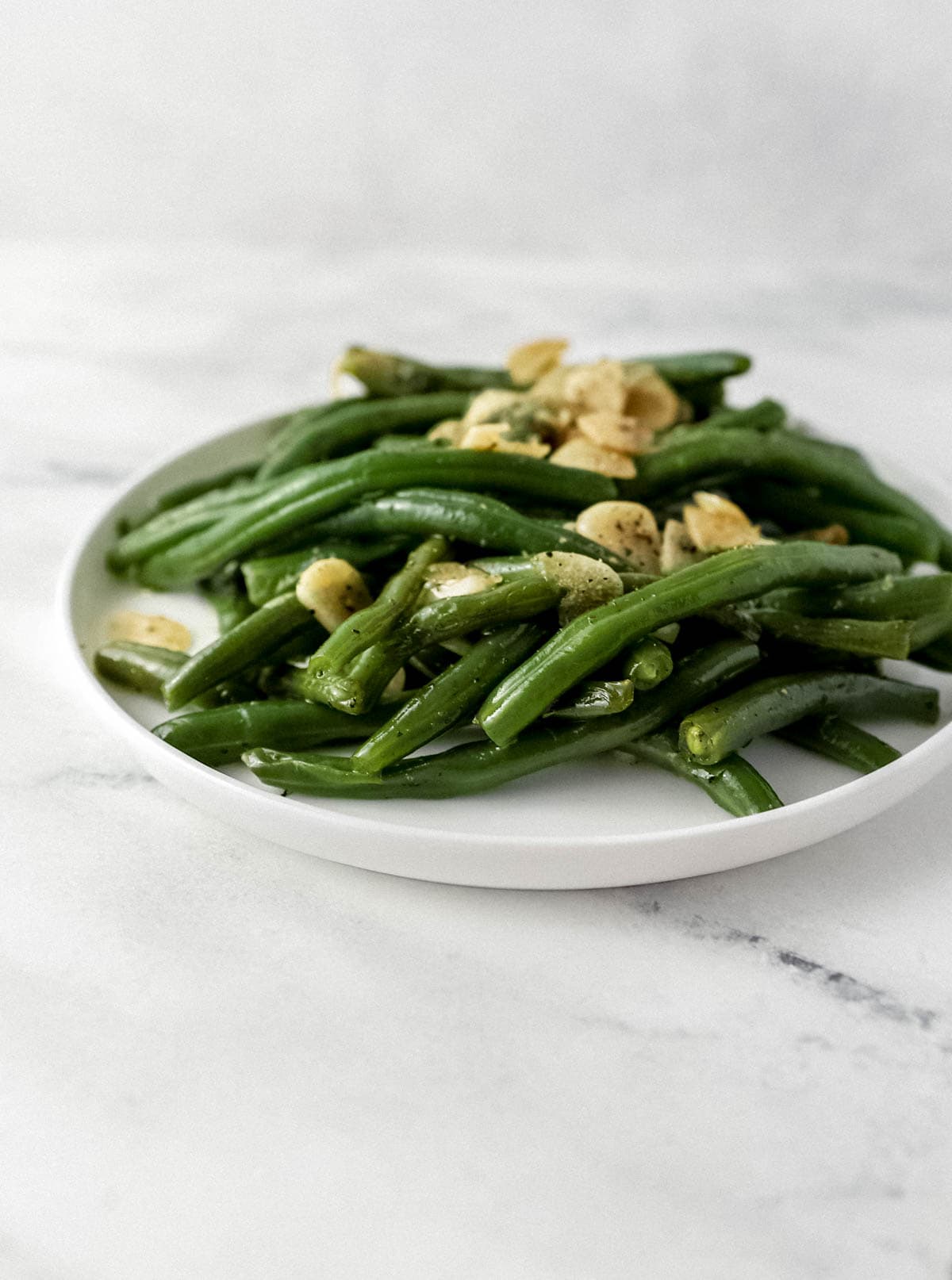 close up side view of green beans on white plate 
