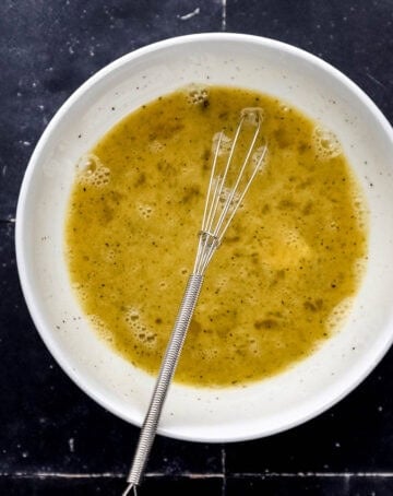 Overhead view of cracked eggs in bowl with whisk.