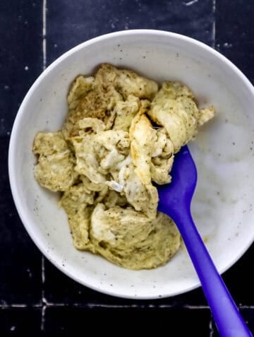 Overhead view of scrambled eggs in white bowl with spatula.