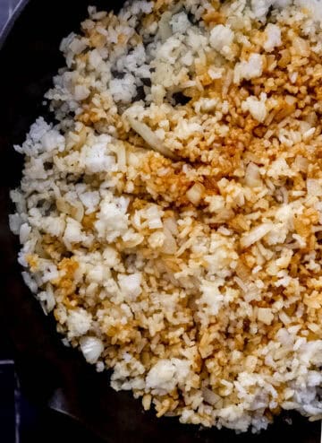 Close up view of rice in cast iron skillet with onion and soy sauce.