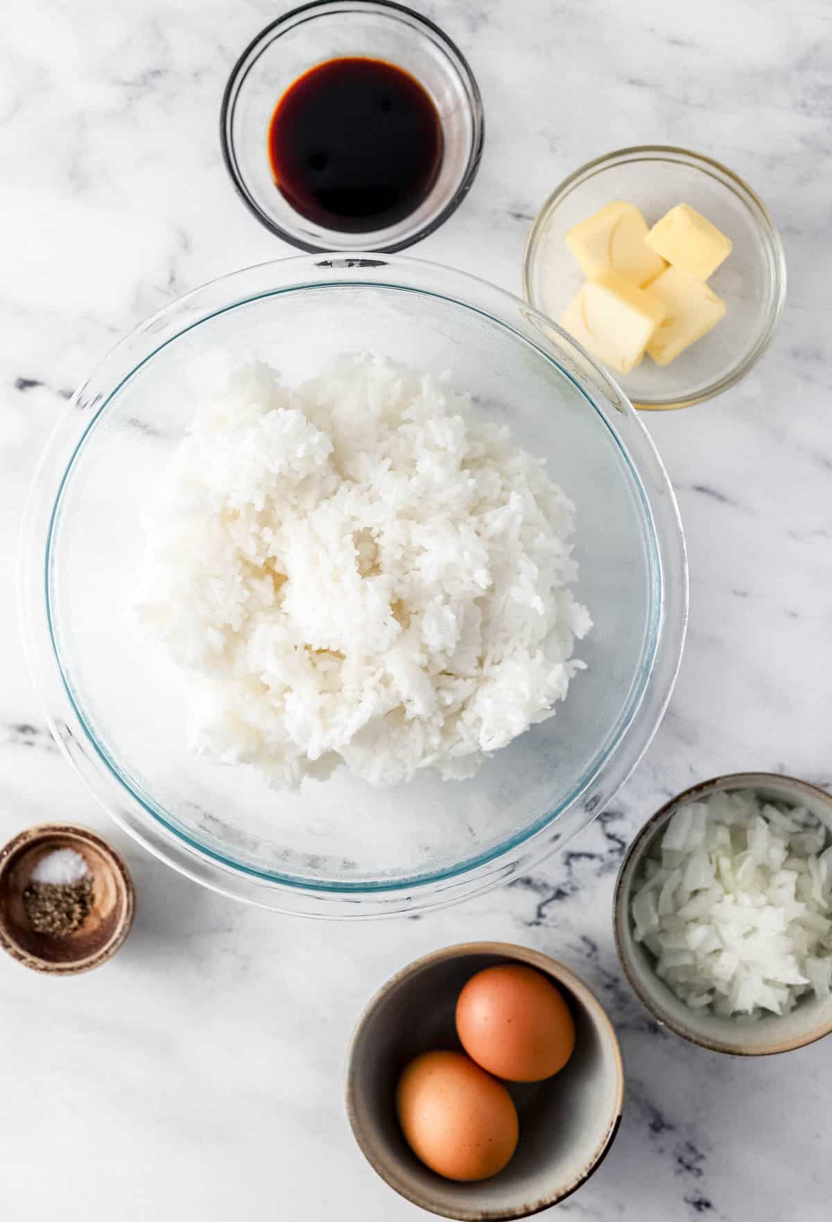 Ingredients needed to make fried rice in separate bowls on marble surface. 