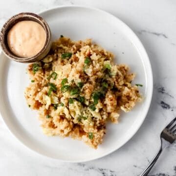 Overhead view of fried rice on white plate with small bowl of sauce on it.