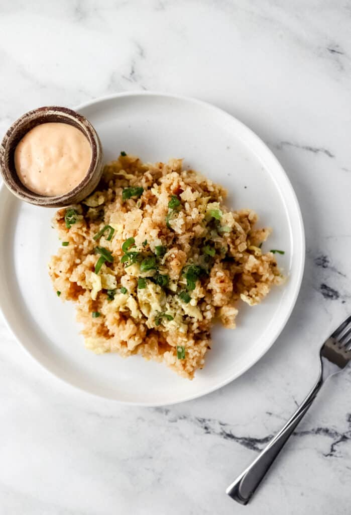 Overhead view of fried rice on white plate with small bowl of sauce on it.