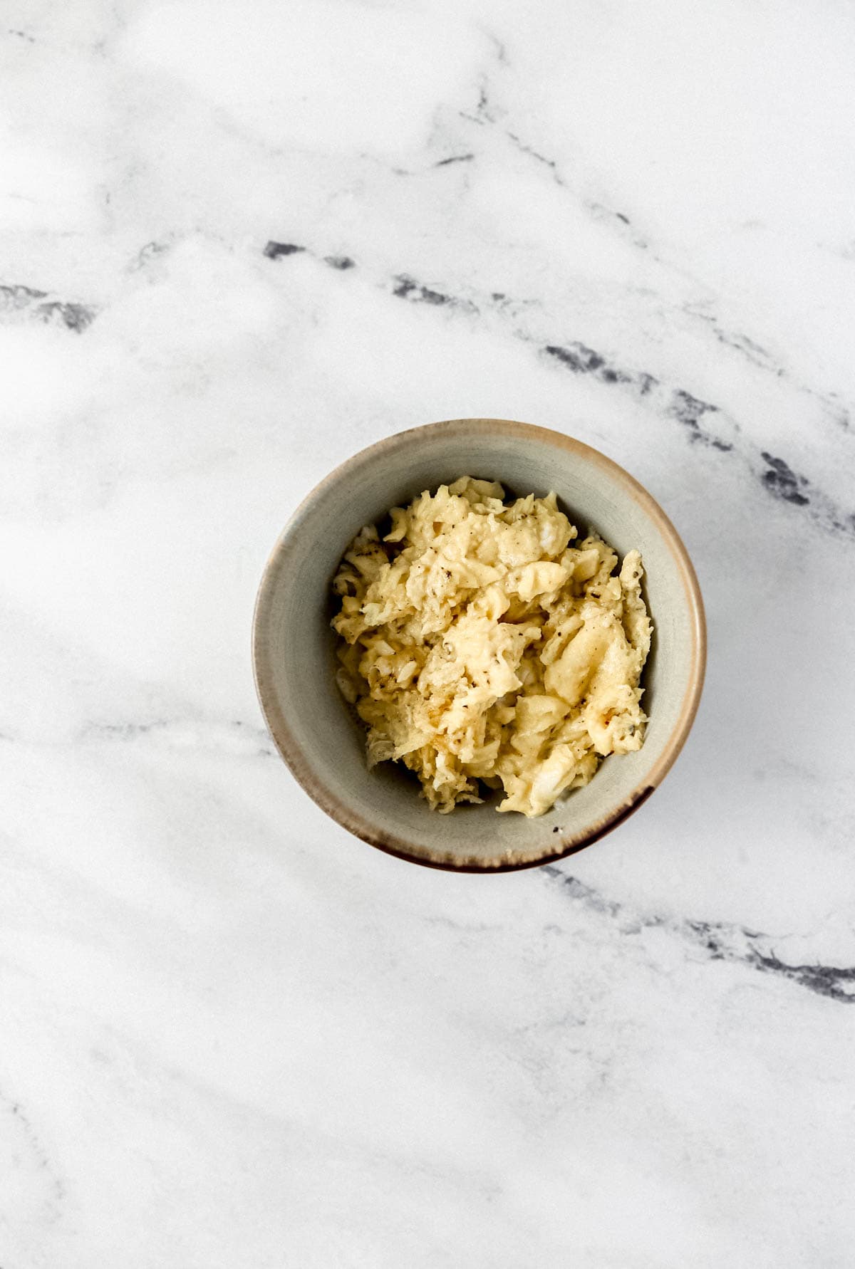 Overhead view of scrambled eggs in small bowl on marble surface. 