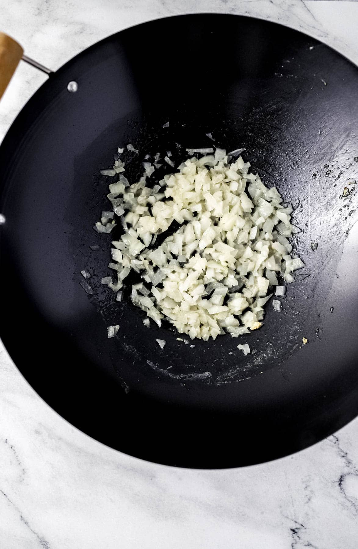 Overhead view of chopped onion and melted butter in a wok.