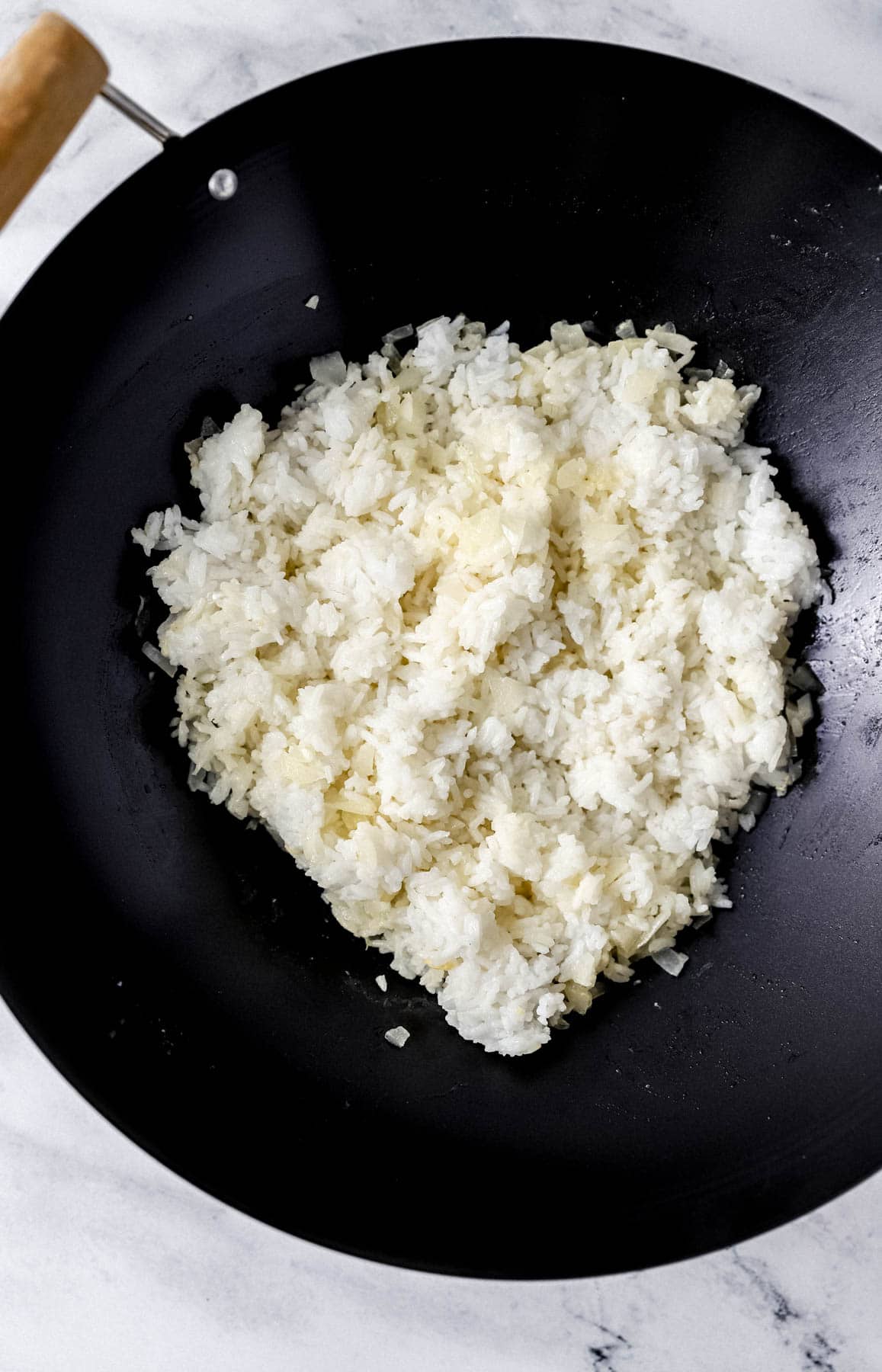 Overhead view of cooked rice added to wok with onion and butter. 