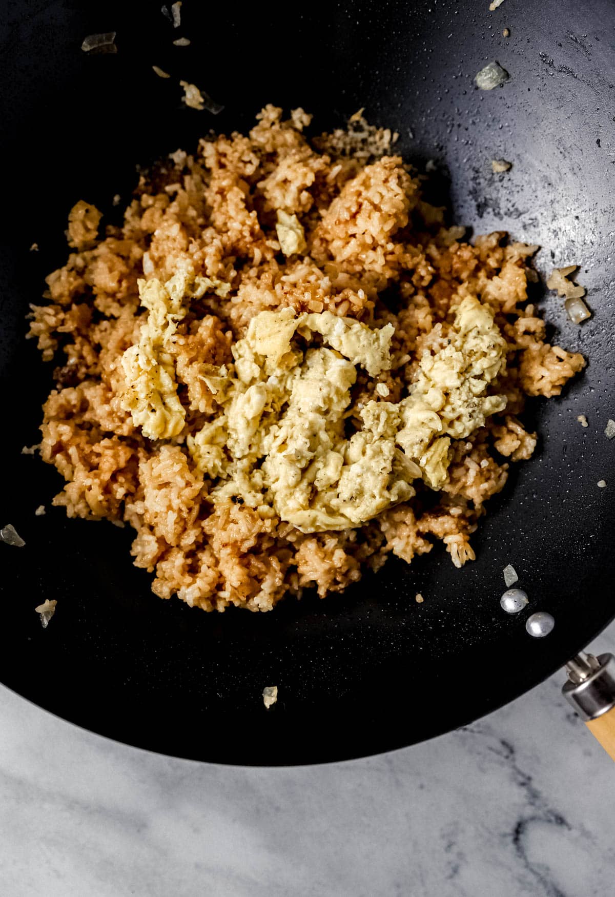 Close up view on scrambled egg added to wok with the rice. 