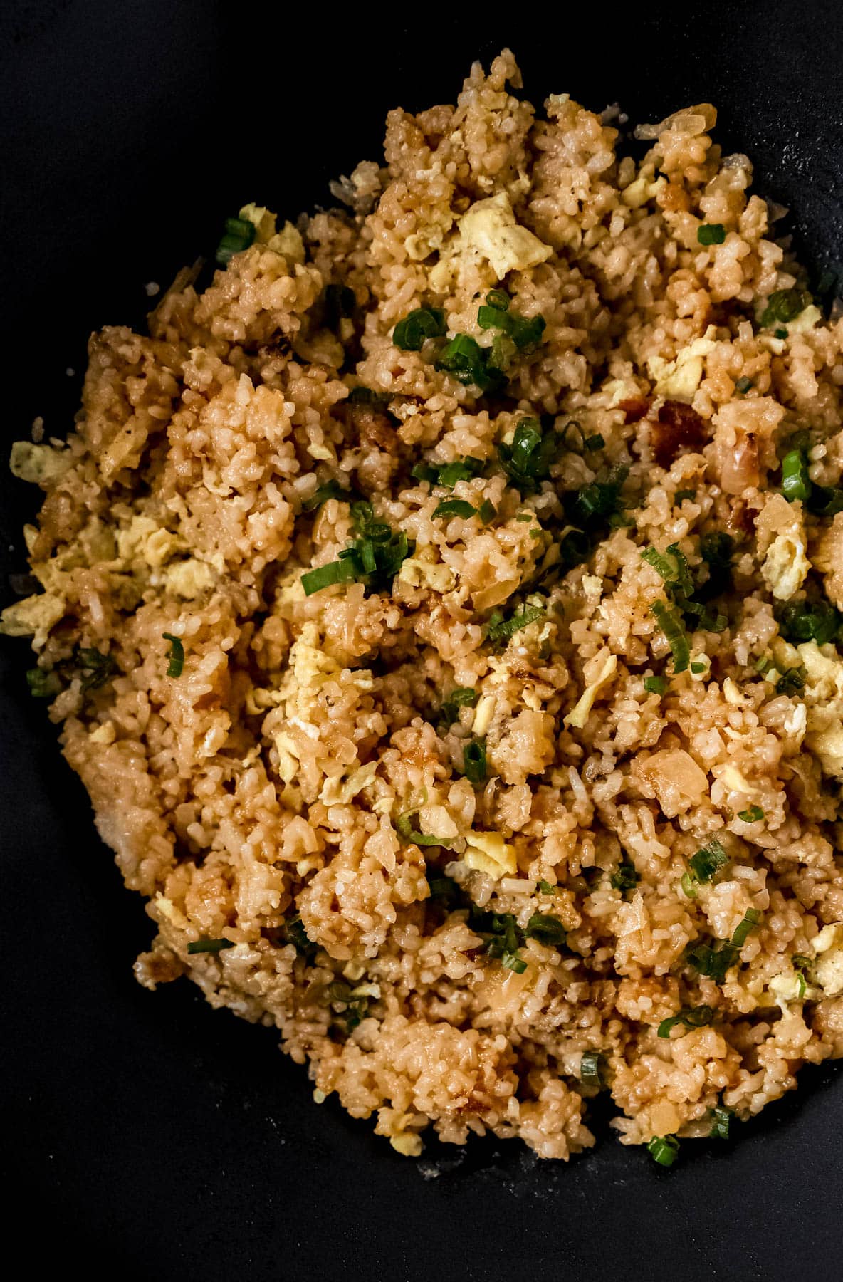 Close up view of finished fried rice in wok topped with some chopped green onion. 