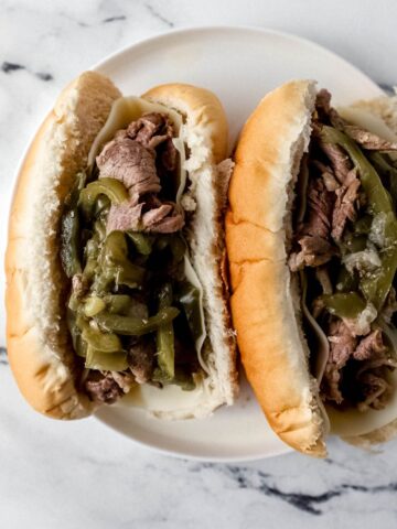 overhead view of two finished cheesesteaks on a white plate on a marble surface