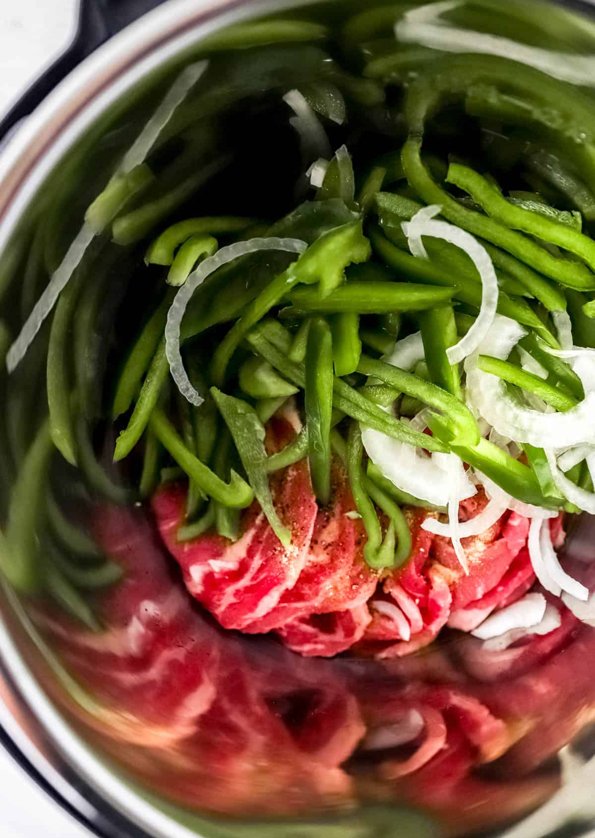 overhead view of cheesesteak ingredients added to an instant pot 