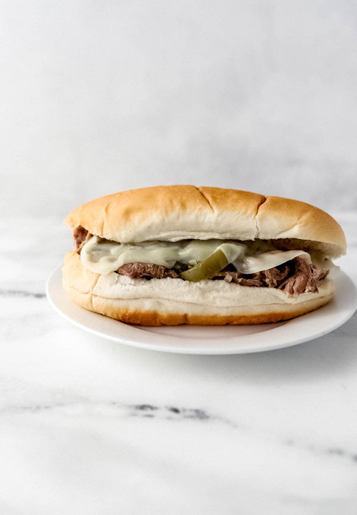 close up side view of finished cheesesteak on white plate 