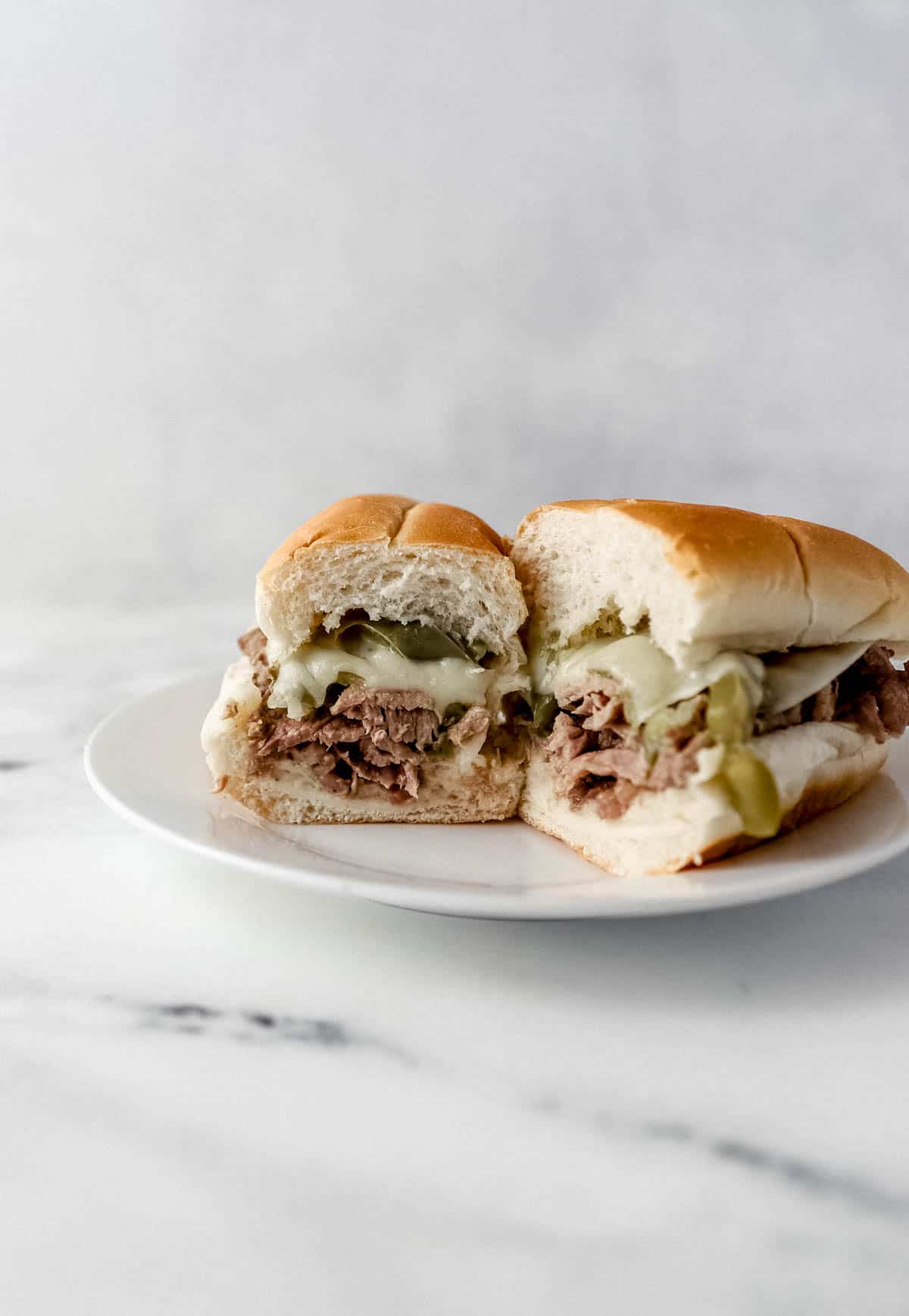 cheesesteak cut in half on white plate on marble surface 