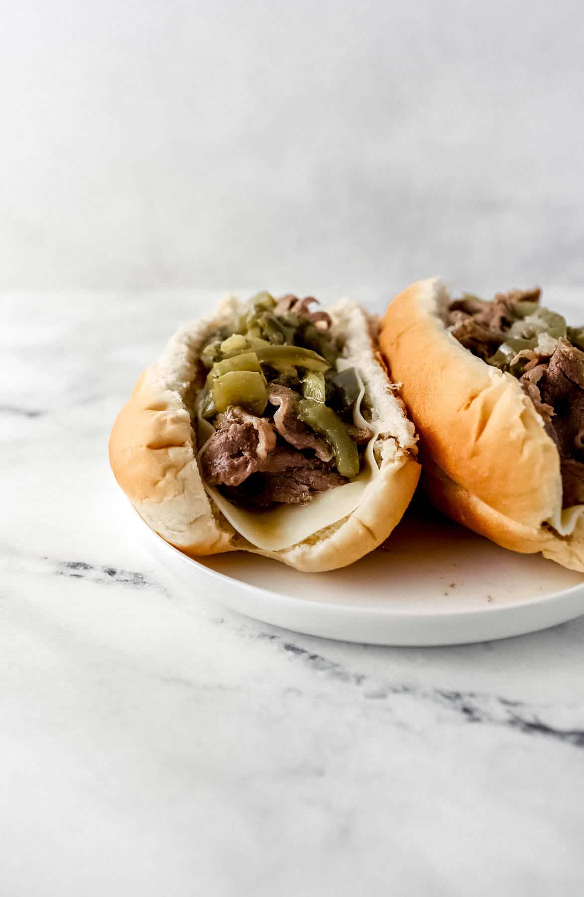 close up front view of two finished cheesesteaks on white plate on marble surface 