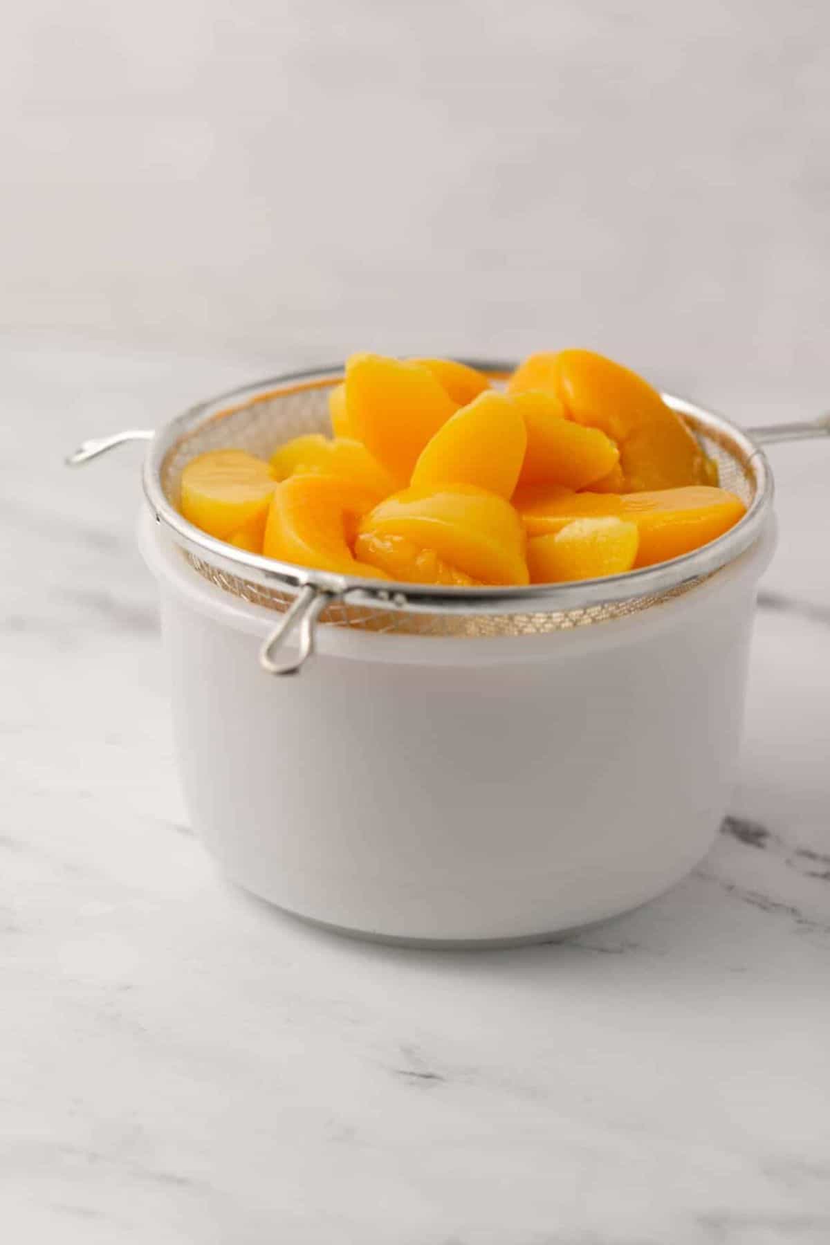 close up side view of white bowl topped with strainer with sliced peaches in it